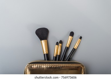 Make Up Brushes Spilling Out Of A Gold Cosmetics Bag On Pastel Color Background.Top View. Flat Lay. Beauty Concept.