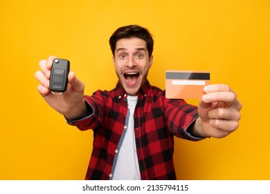 Make Dream Come True. Excited Man Showing New Car Key And Credit Card Buying Automobile Standing On Yellow Orange Studio Background. Auto Loan, Card-Based Payment Transaction And Banking Services