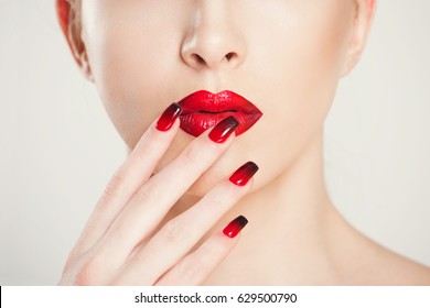 Make up and manicure set. macro cropped image of beautiful gradient of red black manicure and lipstick isolated on white background.