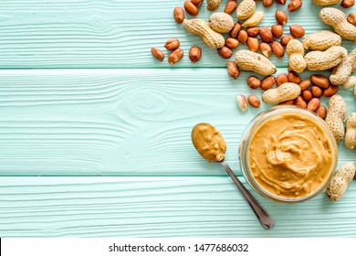 Make peanut butter with paste in glass bowl on mint green wooden background top view copyspace