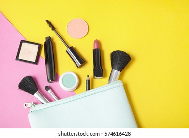 Make Up Products Spilling Out Of A Pastel Blue Cosmetics Bag, On To A Bright Yellow And Pink Background With Empty Space At Side