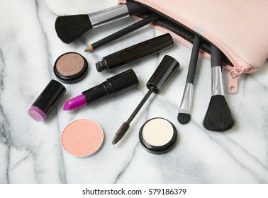 Make Up Products Spilling Out Of A Pastel Pink Cosmetics Bag, On A White Marble Counter Background