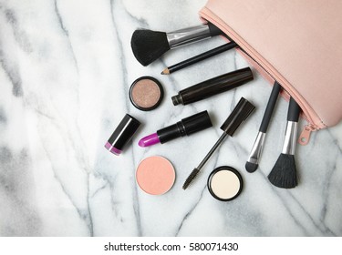 Make Up Products Spilling Out Of A Pastel Pink Cosmetics Bag, On A White Marble Counter Background With Empty Space At Side