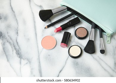 Make Up Products Spilling Out Of A Pastel Blue Cosmetics Bag, On A White Marble Counter Top Background With Blank Space At Side