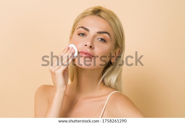 Make up remover. Beautiful woman with a sponge and\
micellar water. Skin care and beauty. Young beautiful woman\
cleaning her face