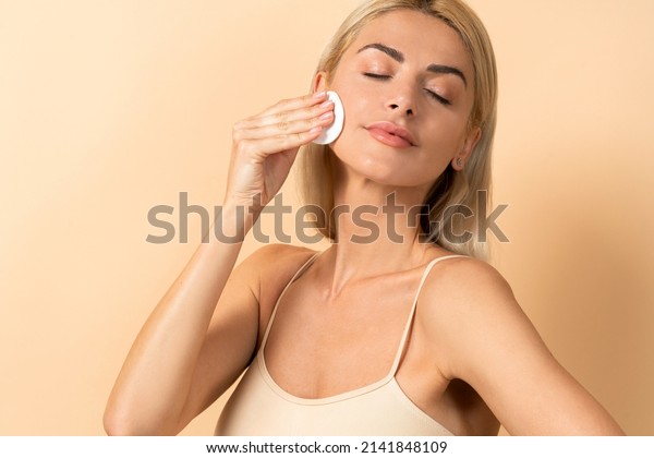 Make up remover. Beautiful woman with a sponge and\
micellar water. Skin care and beauty. Young beautiful woman\
cleaning her face