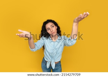 Make Right Choice. Pensive doubtful young woman comparing two variants, making scales with her empty hands and open palms, yellow orange studio background wall, above top high angle overhead view
