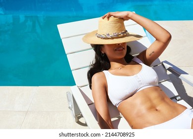 Make sure you have a hat on a sunny day out. Cropped shot of a beautiful young woman relaxing on a lounger by the poolside. - Powered by Shutterstock