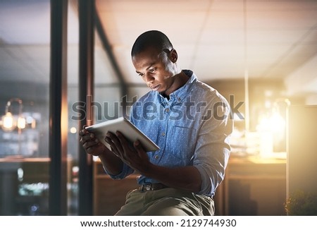 In make things happen mode. Shot of a young businessman using a digital tablet during a late night in a modern office.