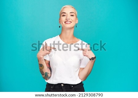 Make it your own. Studio shot of a confident young woman pointing at her t shirt against a turquoise background.