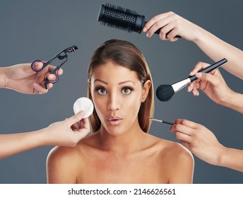 Makeover Madness. Portrait Shot Of A Beautiful Young Woman Getting Her Makeup And Hair Done Against A Grey Background.