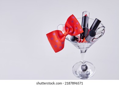 Makeup Accessories And Red Bow Tie In A Cocktail Glass. Isolated On White Background.