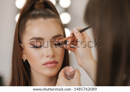 Makeup artist applies eye shadow, perfect evening makeup. Beauty redhead girl with perfect skin and freckles