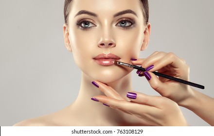 Makeup Artist Applies  Pink Gloss Lipstick  . Beautiful Woman Face. Hand Of Make-up Master, Painting Lips Of Young Beauty  Model Girl . Make Up In Process
