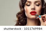  Makeup artist applies  red lipstick  . Beautiful woman face. Hand of make-up master, painting lips of young beauty  model girl . Make up in process