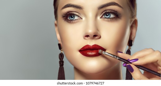 Makeup artist applies red lipstick . Beautiful woman face. Hand of make-up master, painting lips of young beauty model girl . Make up in process