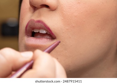 Makeup artist applying dark red lip liner on a model's lips during a makeup session - Powered by Shutterstock