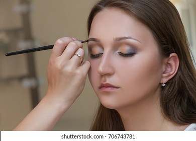 Makeup artist applying eyebrow shadows with beauty brush to the face of a young pretty woman. Bridal make up. - Shutterstock ID 706743781