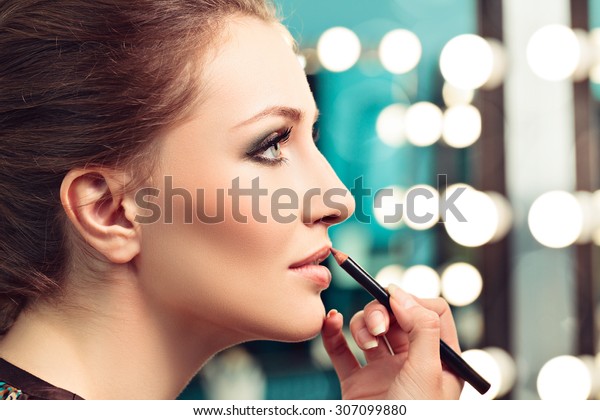 Make-up artist applying lip liner on model's lips,
focus on model's eye