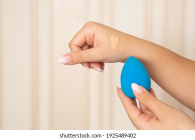 Makeup artist applying liquid foundation with blue beauty blender from her hand. Space for text