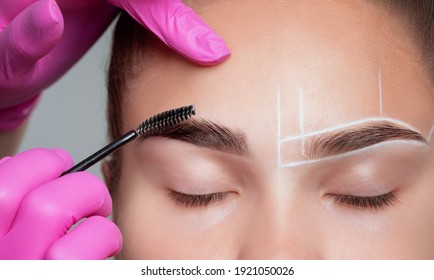 Make-up artist combing eyebrows to a beautiful young woman with clean skin after permanent makeup. Makeup concept, eyebrow shape modeling.