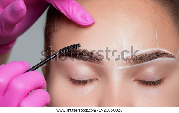 Make-up artist combing eyebrows to a beautiful\
young woman with clean skin after permanent makeup. Makeup concept,\
eyebrow shape modeling.