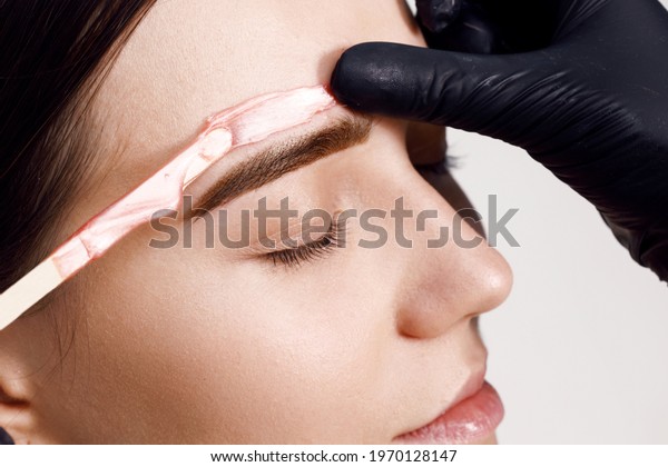 Makeup artist does facial hair removal procedure.\
Styling and lamination of eyebrows. Woman doing eyebrow permanent\
makeup correction. Microblading brow. Melted wax for removing\
facial hair.