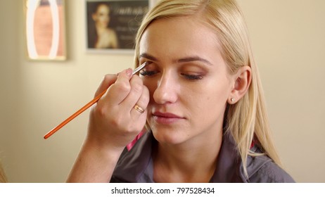 Make-up artist doing professional make-up to young woman in beauty studio. Dressing room.