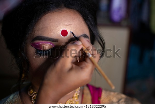 a makeup artist drawing\
a beautiful design called kolka or Bindi in India on the forehead\
of a bride