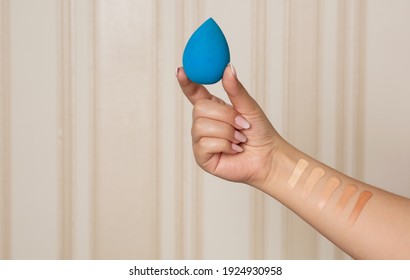 Makeup artist holding blue beauty blender and having swatches of liquid foundation on her hand. Space for text