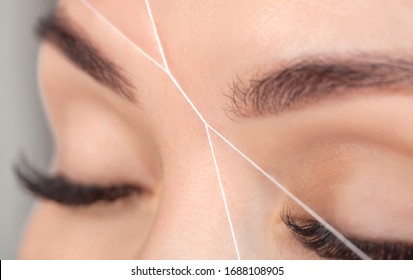The make-up artist plucks eyebrows with a thread close-up. Women's cosmetology in the beauty salon.