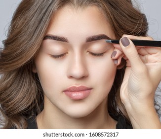 Make-up artist plucks eyebrows with tweezers to a woman with curly brown hair and nude make-up. Beautiful thick eyebrows close up. Professional makeup and cosmetology skin care.