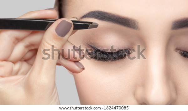 Make-up\
artist plucks eyebrows with tweezers to a woman with curly brown\
hair and nude make-up. Beautiful thick eyebrows close up.\
Professional makeup and cosmetology skin\
care.