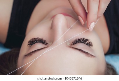 Die Make-up-Künstlerin pflückt sich die Augenbrauen mit einem Faden, Nahaufnahme. Schönheitspflegebehandlungen im Schönheitssalon.