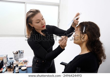 A makeup artist skillfully applying makeup to a client in a beauty studio. The scene shows makeup tools and products on a table, emphasizing professional beauty services and artistry.