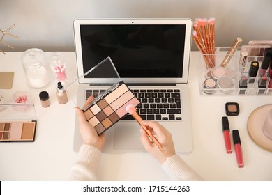 Makeup artist at table with modern laptop and cosmetics