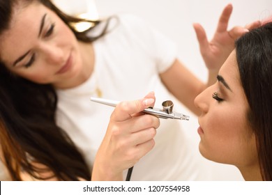 Make-up artist using aerograph making an airbrush make up to an African young woman in a beauty center. Beauty and Aesthetic concepts.