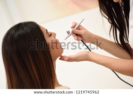 Make-up artist using aerograph making an airbrush make up to an African young woman in a beauty center. Beauty and Aesthetic concepts.