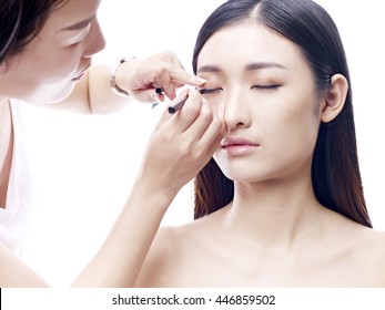 makeup artist working on a beautiful young female asian model, isolated on white background.