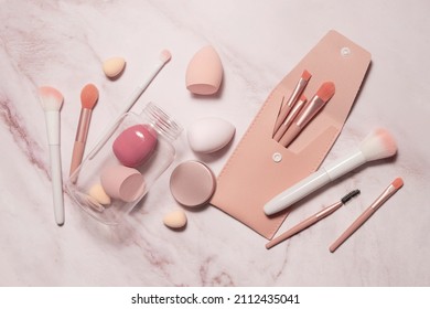 Makeup artist's tools in pink on a marble dressing table: brushes for powder, blush, eyebrows, shadows and sponges for concealer and foundation. - Shutterstock ID 2112435041