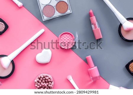 Makeup background with rounge, powder and tools on pink and grey table top view.
