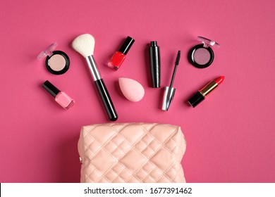 Makeup bag with cosmetic products spilling out on to pastel pink background. Flat lay, top view. Stylish make up artist pouch with professional beauty products