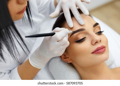 Make-Up. Beautician Hands Doing Eyebrow Tattoo On Woman Face.Permanent Brow Makeup In Beauty Salon. Closeup Of Specialist Doing Eyebrow Tattooing For Female. Cosmetology Treatment. High Resolution
