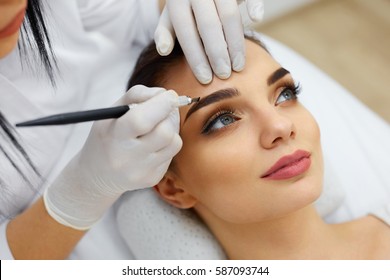 Make-Up. Beautician Hands Doing Eyebrow Tattoo On Woman Face.Permanent Brow Makeup In Beauty Salon. Closeup Of Specialist Doing Eyebrow Tattooing For Female. Cosmetology Treatment. High Resolution 
