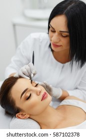 Make-Up. Beautiful Young Woman Receiving Permanent Brow Makeup In Beauty Salon. Closeup Of Beautician Doing Eyebrow Tattoo For Female Face. Cosmetology Treatment. High Resolution 