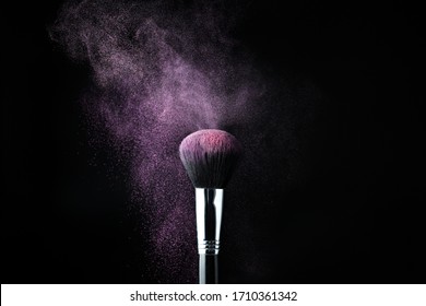 Make-up brush with pink powder splashes explosion on black background. Beauty concept.