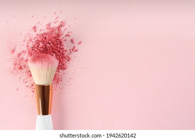 Makeup brush and scattered blush on pink background, top view. Space for text