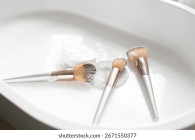 Makeup brushes with cleaning tool and soap in sink, closeup