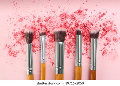 Makeup brushes and scattered eye shadow on pink background, flat lay