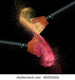 Makeup Concept. Stop Action View Of Two Makeup Brushes Applying Matching Red And Gold Powder Over Black Background